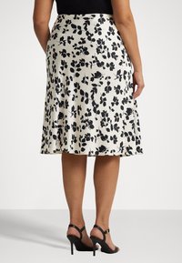 En knälång, vit kjol med ett svart blommönster, gjord av ett glatt tyg. Matchad med svarta, remmade klacksandaler.