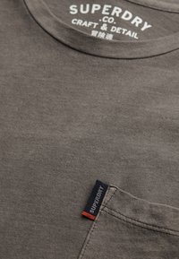 Szara bawełniana koszulka z okrągłym dekoltem, z kieszonką oraz metką z nazwą marki. Gładka faktura i swobodny design.