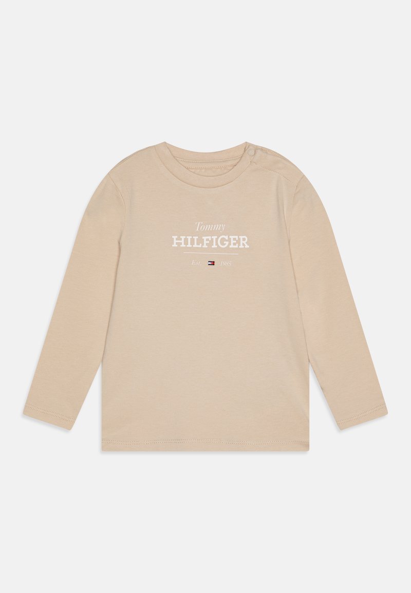 Beige long-sleeve t-shirt made of cotton, featuring "Tommy HILFIGER" text and logo, with a round neck and shoulder snap detail.