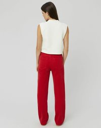 Débardeur blanc sans manches en maille avec un tissu texturé, associé à un pantalon en velours côtelé rouge à taille haute et jambes larges, doté de poches arrière et de coutures visibles.