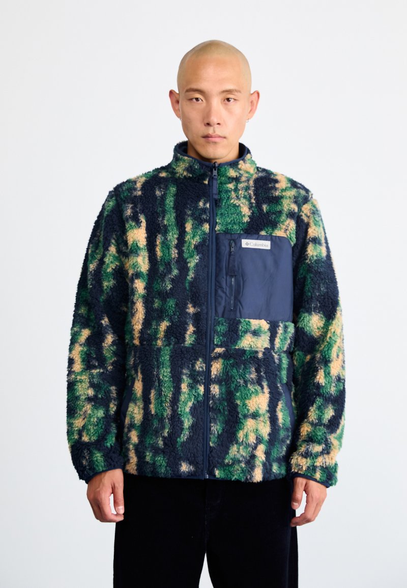 Fleecejacka med ett livfullt mönster i grönt, marinblått och beige, full dragkedja, och en marinblå ficka fram med logopatch. Mjuk, texturerad tyg.