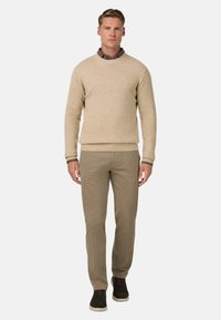 Světlé béžové pletené svetr s kulatým výstřihem, doplněný světle hnědými chinos kalhotami. Model má na sobě tmavě hnědé tenisky. Jednoduchý a čistý design.