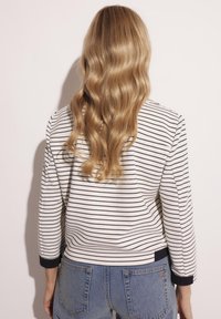 Biały i granatowy sweter w pasy z okrągłym dekoltem, ściągaczami przy mankietach i teksturowanym dzianinowym materiałem; zestawiony z dżinsami o wysokim stanie.