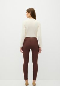 Bruine leggings met een gladde textuur en een aansluitend ontwerp, gecombineerd met een crèmekleurig top met lange mouwen. Minimalistische esthetiek; geen zichtbare patronen.