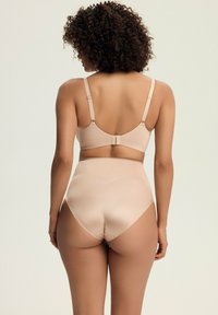 Nagi stanik i zestaw majtek o wysokim stanie z gładkiego materiału, z regulowanymi ramiączkami i bezszwowym designem. Akcenty wykończeniowe są minimalne.