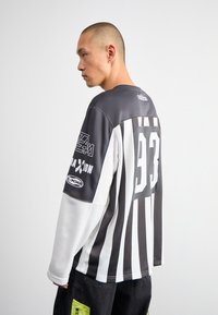 Mustvalge triibuline pikavarsiline jerser, ümmarguse kaelusega, seljal number "93" ja logo aktsendid varrukatel.