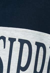 Camicetta a maniche corte blu navy e grigio chiaro con testo audace in blu scuro. Tessuto in cotone morbido e liscio con una banda orizzontale a contrasto.