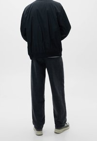 Chaqueta bomber de nailon negra con puños acanalados, combinada con pantalones vaqueros oscuros de talle alto y zapatillas de color claro con suelas texturizadas.