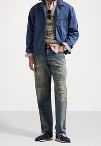 Jeansjacka, beige mönstrad tröja, rosa skjorta, slitna blå jeans och marinblå sneakers kompletterar outfiten. Tillbehören inkluderar solglasögon och en klocka.