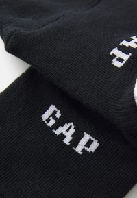 Crne pletene čarape s bijelim "GAP" logotipom. Mekani materijal s rebrastim uzorkom i dizajnom do gležnja.