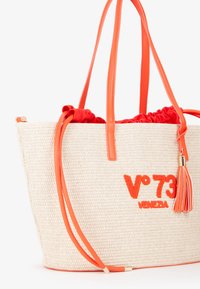 Borsa a tracolla di paglia intrecciata con dettagli in pelle arancione, presenta un interno con cordoncino rosso e una decorazione a pon-pon. Logo "V°73 VENEZIA" ben visibile.