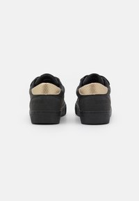 Sneaker nere con tessuto nero texturizzato, dettagli beige a motivo serpente in contrasto sul tallone e una suola in gomma nera monotona.
