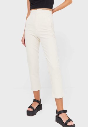 Pantalons crème taille haute à coupe droite, avec poches latérales et texture lisse. Associés à des sandales noires épaisses.