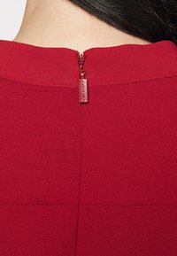 Vestido rojo con una textura suave y una cremallera visible en la parte posterior, con un pequeño tirador de metal con la marca.