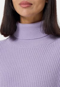 Pull à col roulé en lavande clair avec un motif tricoté texturé. Présente un col haut et un tissu doux, mettant en valeur une coupe ajustée.