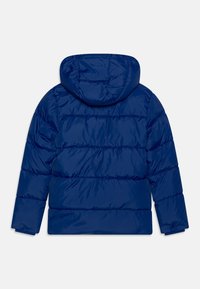 Modrá péřová bunda s kapucí. Má prošívaný design, lesklý povrch a elastické manžety. Pohled zezadu ukazuje vodorovné prošití a hladkou texturu.