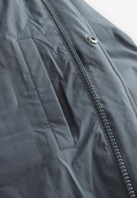 Dunkelgrau jacket aus einem glatten, leicht glänzenden Stoff, mit einem vorderen Reißverschluss und einer Klappentasche mit genähten Details.