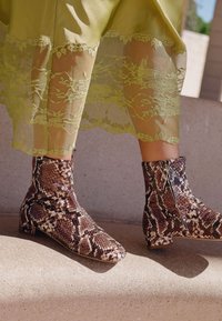 Bruna och cremefärgade ankelstövlar med ormskinnsmönster och låg klossklack, utrustade med en sidodragkedja och en mjuk, blank yta.