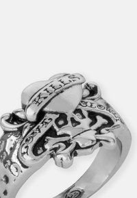 Srebrni prsten s dizajnom lubanje i ukrštenih kostiju, s natpisom "Ubija" na traku. Detaljna tekstura i polirana površina.