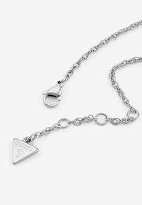 Collana con catena d'argento con un ciondolo triangolare inciso con "GUESS", dotata di chiusura a moschettone e design a catena con maglie rotonde.