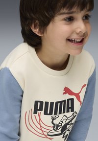 Sudadera crema y azul con el logotipo de Puma y una impresión gráfica de una zapatilla, hecha de suave tejido de algodón. Cuello redondo, mangas largas.
