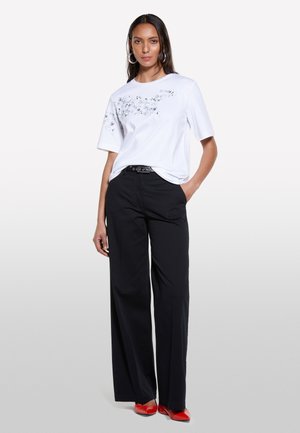 T-shirt blanc à manches courtes avec des embellissements floraux, associé à un pantalon large noir et des escarpins rouges, arborant une ceinture noire.
