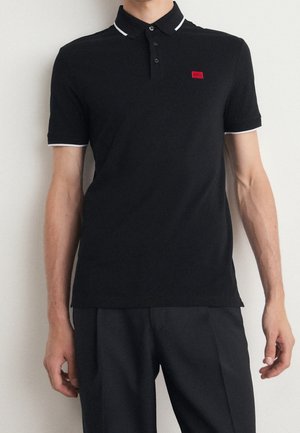 Polo negro con ribete blanco en el cuello y las mangas, que presenta un pequeño logo rojo en el pecho. Hecho de algodón, ajustado al cuerpo.