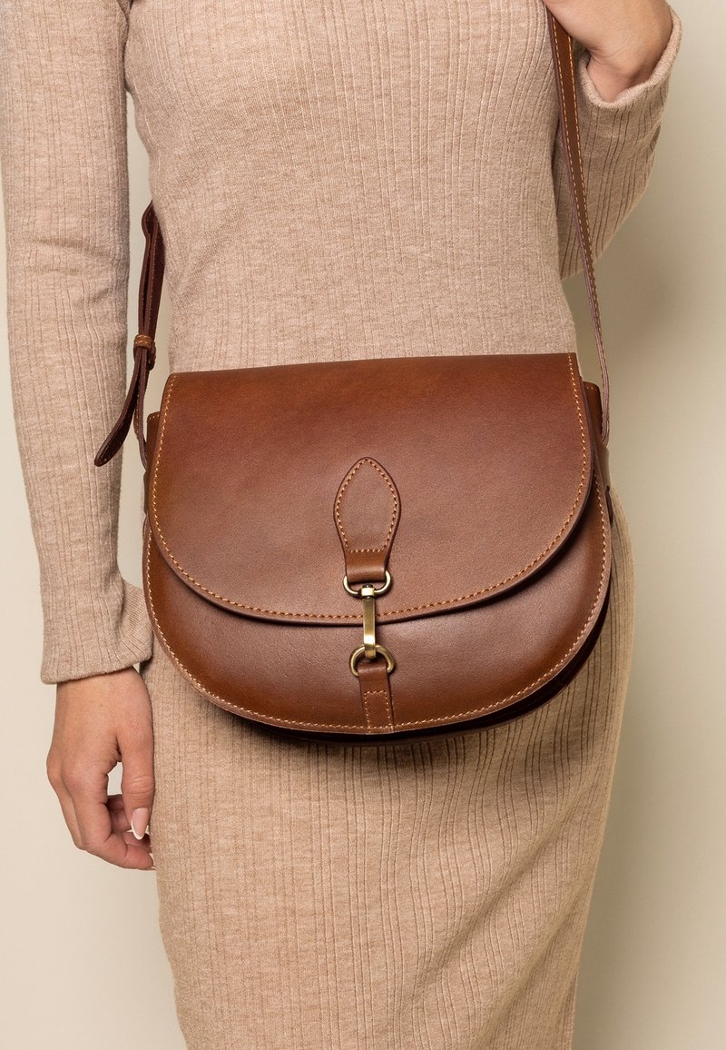 Borsa a tracolla in pelle marrone con forma arrotondata, dotata di chiusura a pattina, accessori in ottone e una tracolla intrecciata. Texture liscia con dettagli di cucitura.