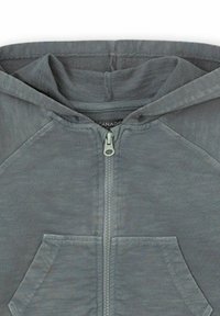 Sudadera gris con cremallera, bolsillo frontal y capucha, con el tirador de la cremallera centrado y la textura de la tela visible.