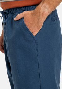 Tmavě modré jogger kalhoty ze směsi bavlny s elastickým pasem a stahovací šňůrkou, které mají boční kapsy a volnější střih.