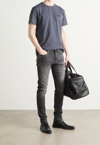 Šedé tričko, tmavé džíny a černé kožené boty. Nese černou koženou tašku s kruhovým kovovým detailem. Jednoduchý a moderní styl.