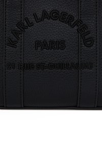 Čierna textúrovaná kožená sekcia s embosovaným čiernym textom, ktorý znie "KARL LAGERFELD PARIS 21 RUE ST-GUILLAUME."