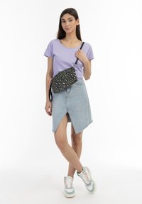 Borsa verde con stampa leopardata e tracolla nera, indossata sopra un top lavanda e una gonna di jeans azzurri chiari con spacco frontale, abbinata a sneakers multicolori.