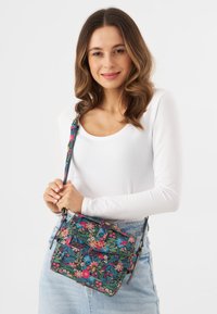 Borsa a tracolla floreale con sfondo blu scuro, fiori rosa e verdi vivaci, tracolla regolabile e chiusura a pattina.