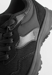 Czarne buty sportowe z siateczki, zamszu i błyszczącymi akcentami. Posiadają teksturowaną powierzchnię, wyściółkę na języku oraz gumową podeszwę z przyczepnością.