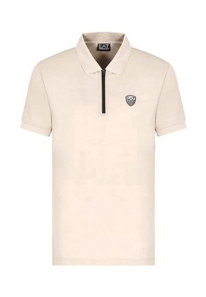 Polo shirt beige a maniche corte realizzato in tessuto morbido, presenta un colletto con zip e un patch logo nero sul lato sinistro del petto.