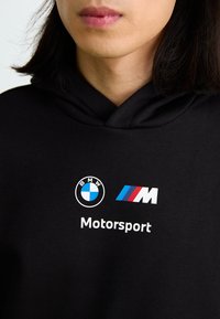 Sort hættetrøje med BMW og Motorsport logoer i hvid og blå. Stofstofet ser glat ud med en afslappet pasform. Justerbar hætte med snore.