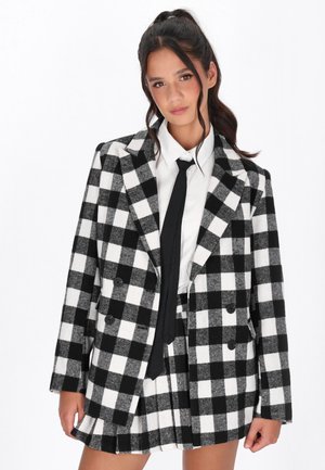 Blazer a scacchi bianco e nero con bottoni doppi, abbinato a una camicia bianca e cravatta nera, in tessuto di lana texture.