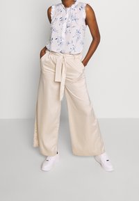 Blusa floreale azzurro chiaro con volant e pantaloni palazzo in raso crema legati in vita, abbinati a sneakers bianche.