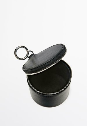 Custodia rotonda nera in pelle con zip e portachiavi, aperta per mostrare l'interno vuoto su sfondo bianco.