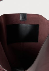 Mauve värvi nahast kott, mille sisemus on kaetud sileda musta nahaplaadiga, pehme sametise tekstuuriga ja struktuurse kujuga. Üksiku nööpkinnitusega ülaosas.