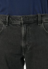 Jeans de mezclilla negra con un diseño clásico de cinco bolsillos, que presentan una textura suave, presillas para cinturón y un cierre de botón en la cintura.