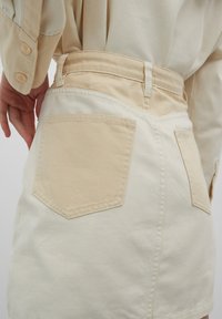 Beige denim rok met een hoge taille, twee achterzakken met contrasterende beige patches en contrasterende stikdetails.
