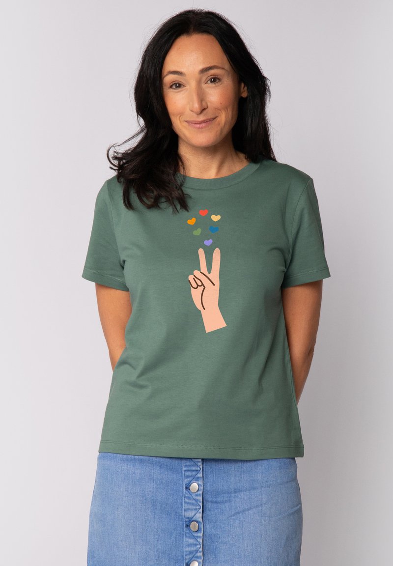 Groene katoenen t-shirt met een perzikkleurige hand die een vredesteken maakt, versierd met meerkleurige hartjes erboven. Korte mouwen, ronde hals.
