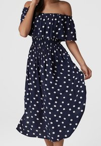 Námořnické off-shoulder šaty s bílými puntíky, smockovaný pas, splývavá sukně, krátké rukávy a lehký materiál. Ideální pro teplé počasí.