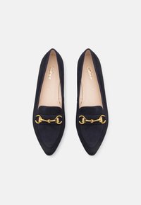 Une paire de mocassins en daim bleu marine à bout pointu avec détail en bit épicene doré et semelles beiges, taille 5, sur fond blanc.