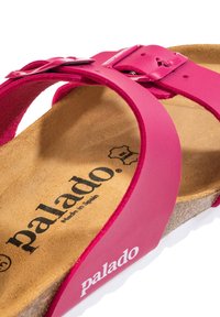 Rosa gummisandaler med en korkfotbädd; har en justerbar metallspänne och en texturerad yta för grepp. Märket "palado" synligt.