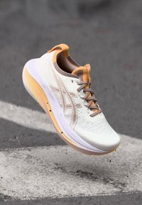 Weiße und hellorange Sportauswahl mit einer strukturierten Oberseite, erhöhter Sohle und minimalistischem Design. Verfügt über das Asics-Logo und eine Schnürverschluss.