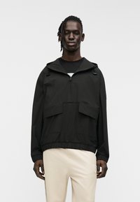 Μαύρο φούτερ με κουκούλα, με δύο τσέπες στο μπροστινό μέρος, φερμουάρ στο λαιμό και ελαστική μέση. Λείο, ελαφρύ  ύφασμα.