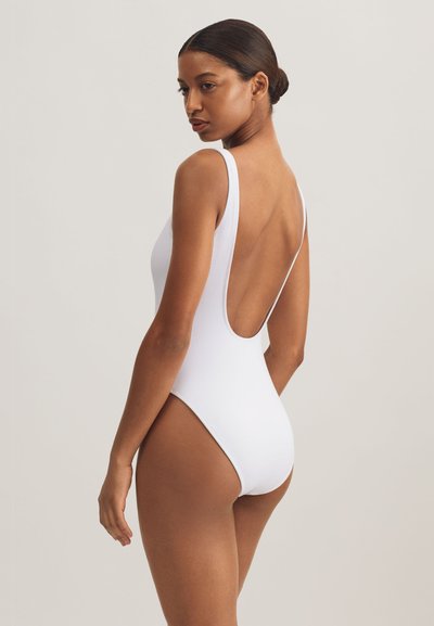 Vit baddräkt med låg rygg, breda axelband och en mjuk, elastisk struktur.